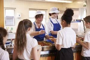 Children in a school being served lunch by chefs