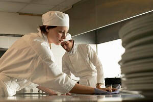 Female and Male Food Service Assistant cleaning a surface in commercial kitchen. 