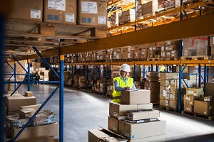 Being a Warehouse Operative  - Female Warehouse Operative leaning on a stack of boxes writing 